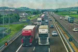 Traffico di camion e automobili su un'autostrada che attraversa una zona rurale e industriale.