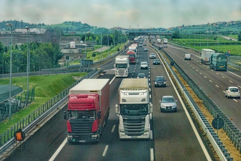Traffico di camion e automobili su un'autostrada che attraversa una zona rurale e industriale.