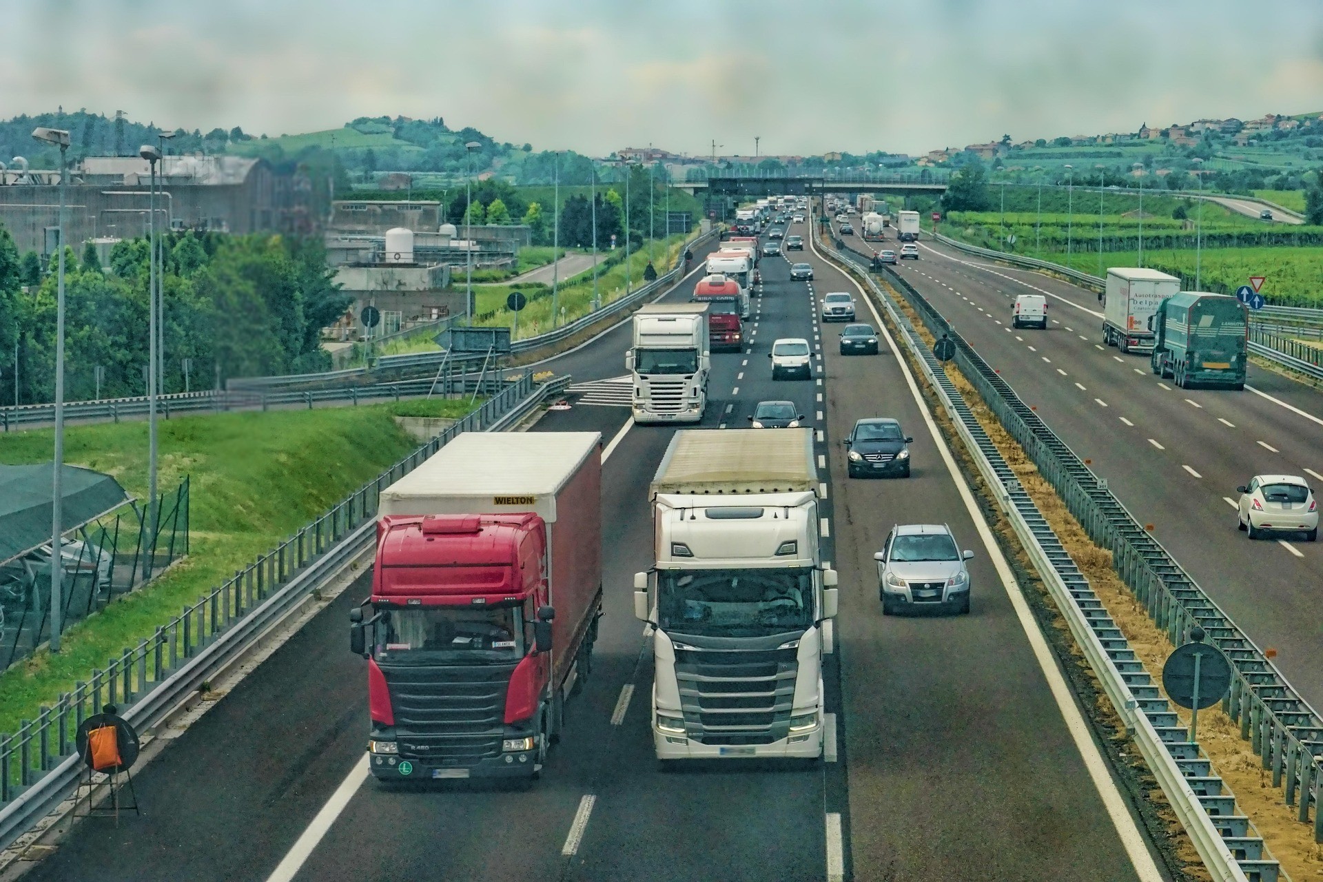 Traffico di camion e automobili su un'autostrada che attraversa una zona rurale e industriale.