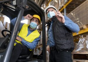Lavoratori con mascherina che discutono, uno seduto su muletto l'altro in piedi al suo fianco